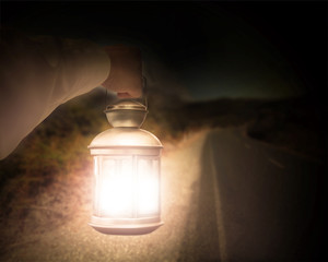 Hand holding light illuminating dark road at night