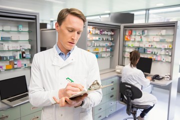 Focused pharmacist writing on clipboard - Powered by Adobe