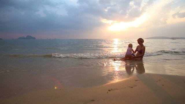 blonde baby girl in purple swimsuit play with her mother sit dow
