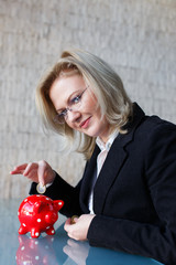 Businesswoman put one euro into red dotted piggy bank