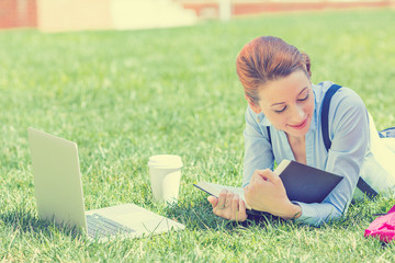 Student studying in park reading book working on computer