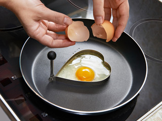 Woman preparing fried eggs in heart form