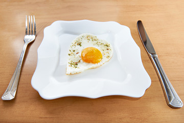 Fried eggs in a heart shape on a white plate and cutlery