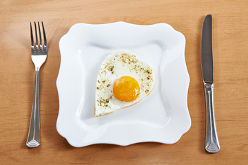 Fried eggs in a heart shape on a white plate and cutlery