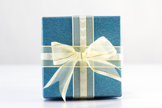 Gold ribbon and bow on top of blue gift box on white background