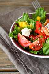 Salad with tomatoes, cheese and greens in a bowl on napkin