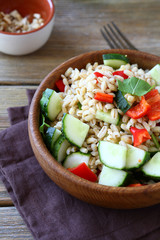 Tasty pearl barley salad with vegetables in a wooden bowl