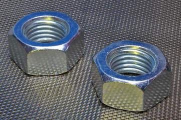 Two steel nuts on metal surface with holes