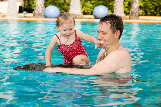 Active father teaching his toddler daughter to swim in pool