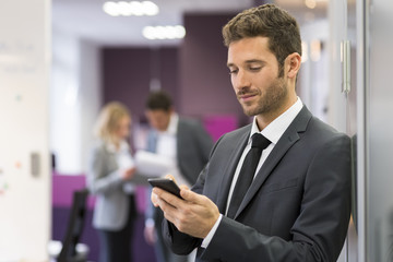 Businessman typing a message on smart-phone in modern office