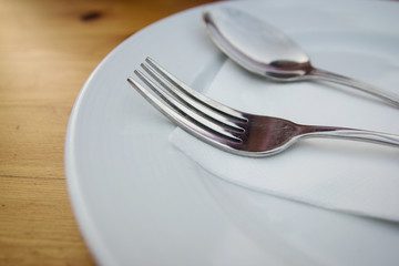 fork and spoon with white plate on wood table