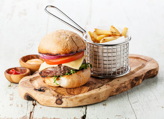 Burger with meat and French fries in basket on wooden background