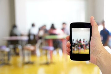 Hand hold smartphone with blured classroom as background
