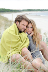 Couple relaxing on windy autumn day on the beach - sea, blanket
