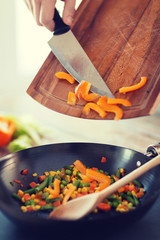 close up of male hand adding peppers to wok