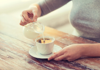 Obraz na płótnie Canvas close up of female pouring milk into coffee