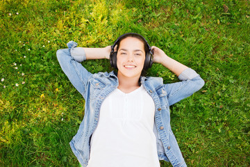smiling young girl in headphones lying on grass