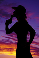 silhouette of woman cowboy hat with gun blow close sunset