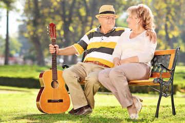 Mature man sitting with his wife in park and holding guitar