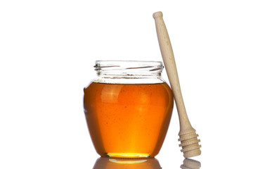 Glass jar of honey with wooden drizzler on a white background.