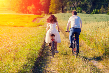 Young happy bride and groom ride bicycles in the meadow