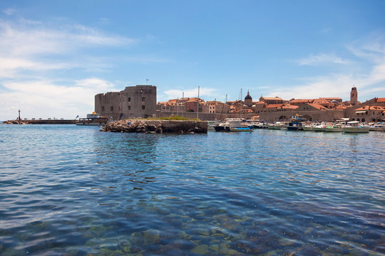 Small boats in city port with St. John fortress in background.