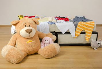 Bear toy on a bed with different colorful newborn clothes