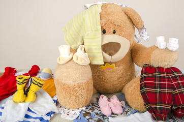 Bear toy on a bed with different colorful newborn clothes