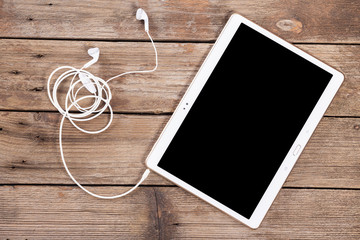 Tablet computer with earphones against wooden background