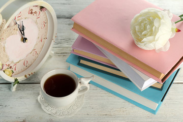 Cup of tea with books and clock on wooden background