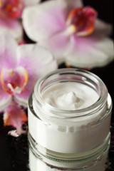 Face cream with orchid flowers on dark background