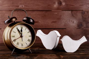Retro clock with decorative birds on table on wooden background