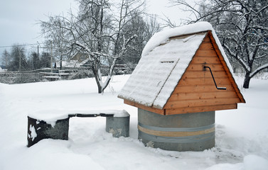 Колодец во дворе деревенского дома под снегом зимним днем