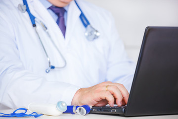 Doctor in white coat using laptop.