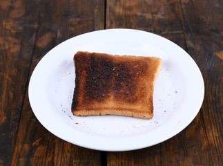 Burnt toast bread on plate, on wooden table background