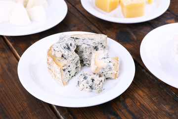 Various types of cheese on plates on wooden table background
