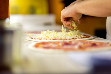 Closeup of chef baker in white uniform making pizza at kitchen