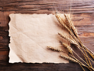 Fototapeta na wymiar Spikelets of wheat with paper on wooden background