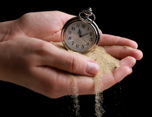 Silver pocket clock in hands and sand flowing away