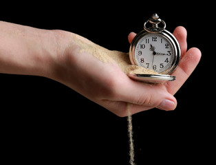 Silver pocket clock in hands and sand flowing away