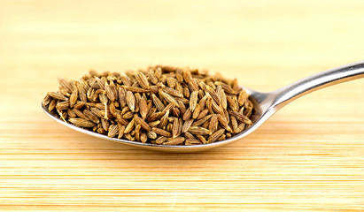 Spoonful of cumin seeds against wooden background