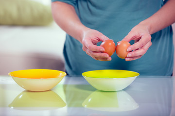 Female hands separating yolk and white of a cracked egg