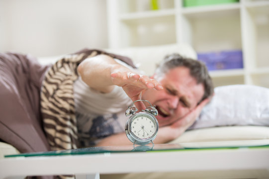 Man lying in bed turning off an alarm clock in the morning.