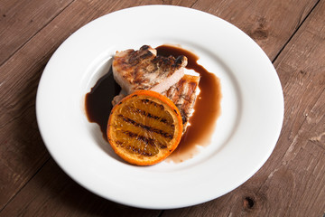 Grilled meat with orange on white ceramic plate on old wooden ta