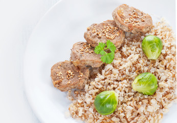 Medallions and brown rice with brussels sprouts on white wood