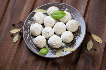 Ceramic plate with raw khinkali over rustic wooden background