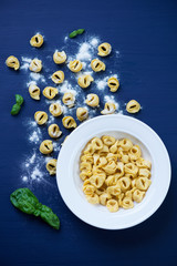 Raw tortellini with flour and green basil, view from above
