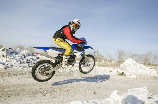 MX winter rider soars from a hill looking back