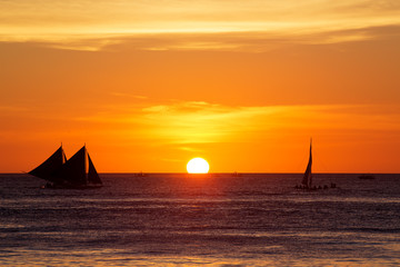 Fototapeta premium Sailboats at sunset on a tropical sea. Silhouette photo.