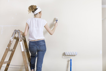 Frau streicht Wand auf Leiter - 76453838